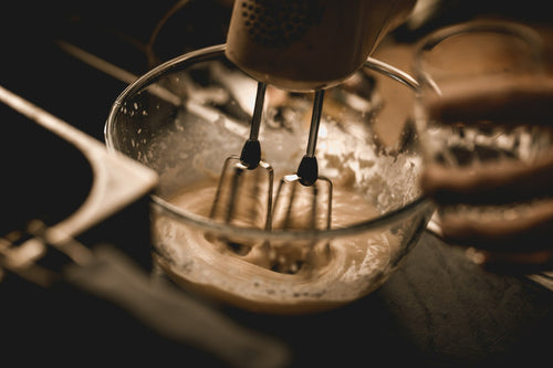 Electric hand mixer whisking batter in a glass bowl